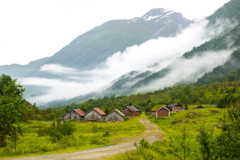 Landscape,With,Old,Wooden,Houses,And,Mountains,Covered,By,Clouds,